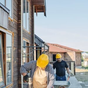 Two workers in hard hats engaged in carpentry at a construction site, building a wooden house.